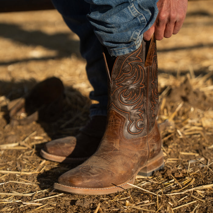 Brown cowboy boot with intricate patterns on a dirt ground