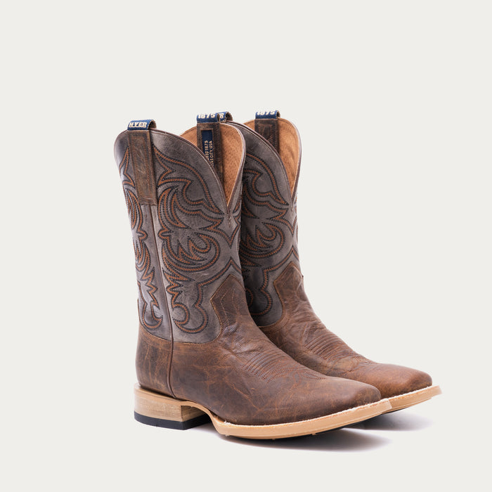 Pair of brown cowboy boots with tan and black intricate stitching on a light gray background