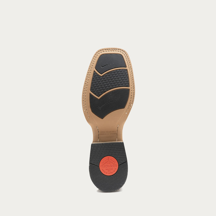 The outsole of a boot is shown from the bottom, featuring a tan rubber footbed, black textured rubber tread, and a small red circular logo on the heel.