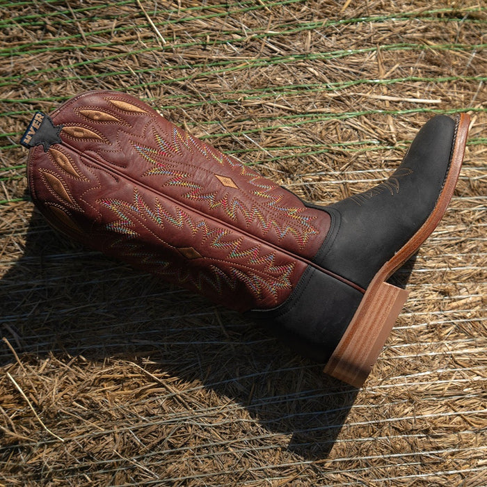 Lifestyle shot of red and black cowgirl boot with multicolor detailed stitching laying on a bed of hay