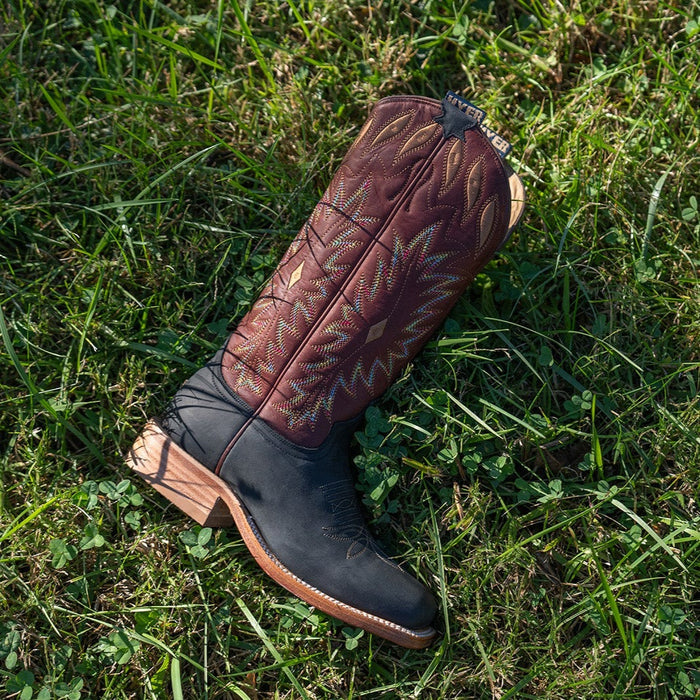 Lifestyle shot of red and black cowgirl boot with multicolor detailed stitching laying on a patch of grass