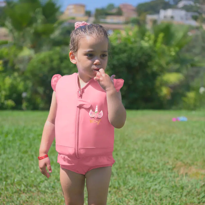 Une petite fille porte le maillot de bain flottant Rosy rose avec une licorne dessinée sur le devant