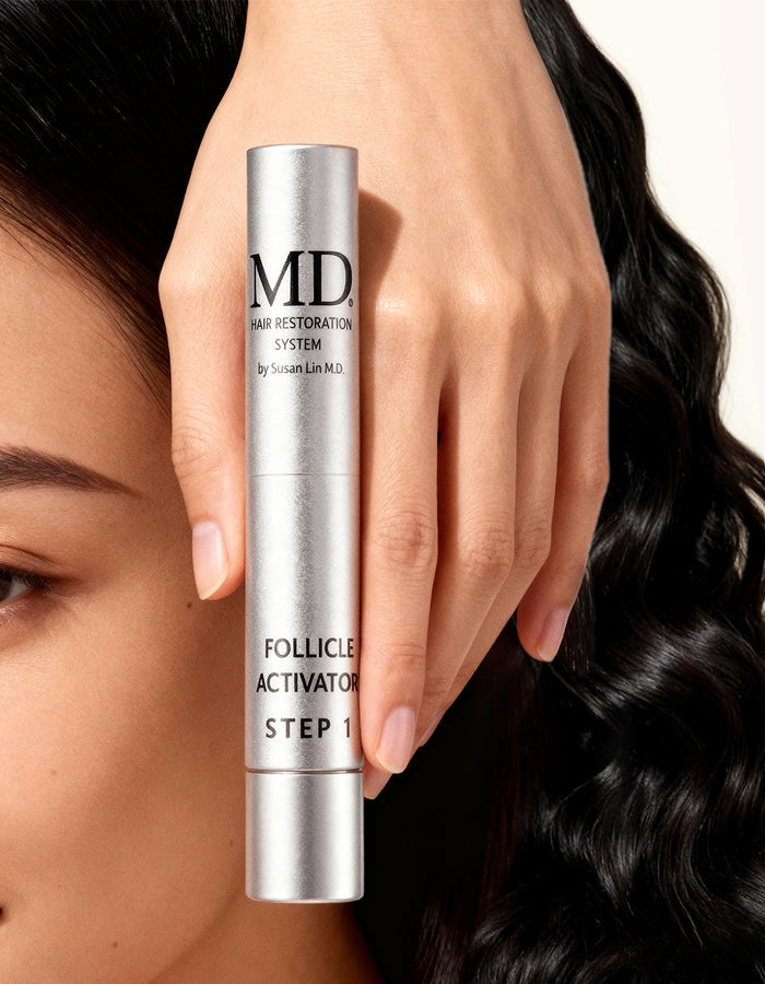 Hand holding MD® Follicle Activator Step 1 scalp serum beside glossy dark wavy hair