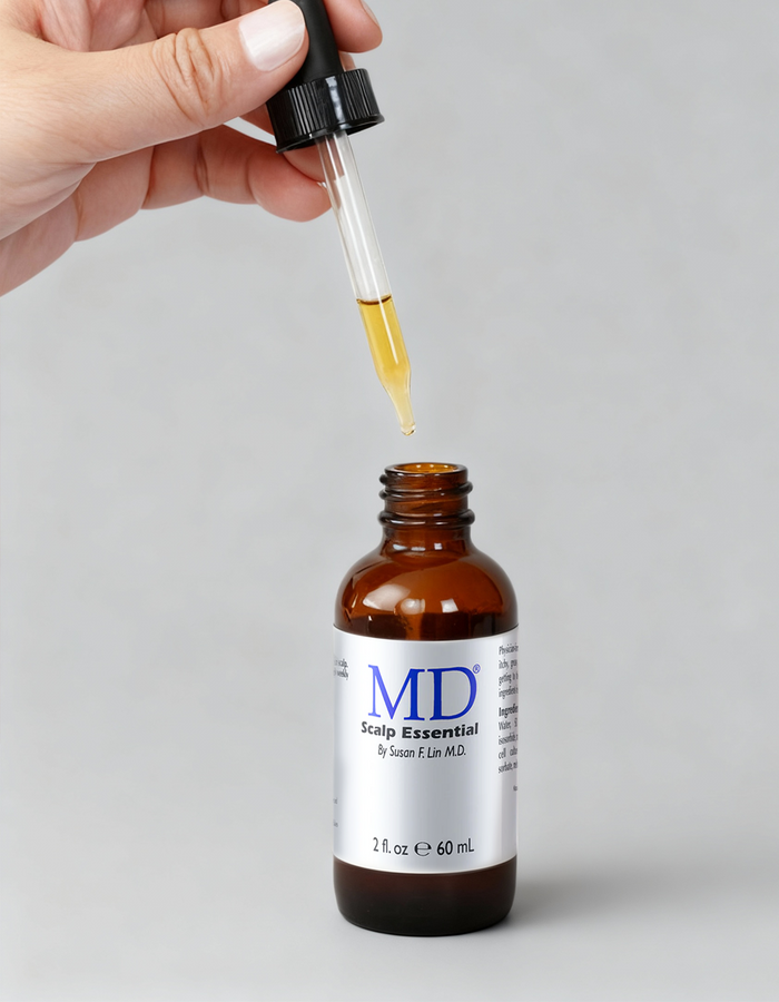 Hand holding the dropper above an open bottle of MD® Scalp Essential scalp serum