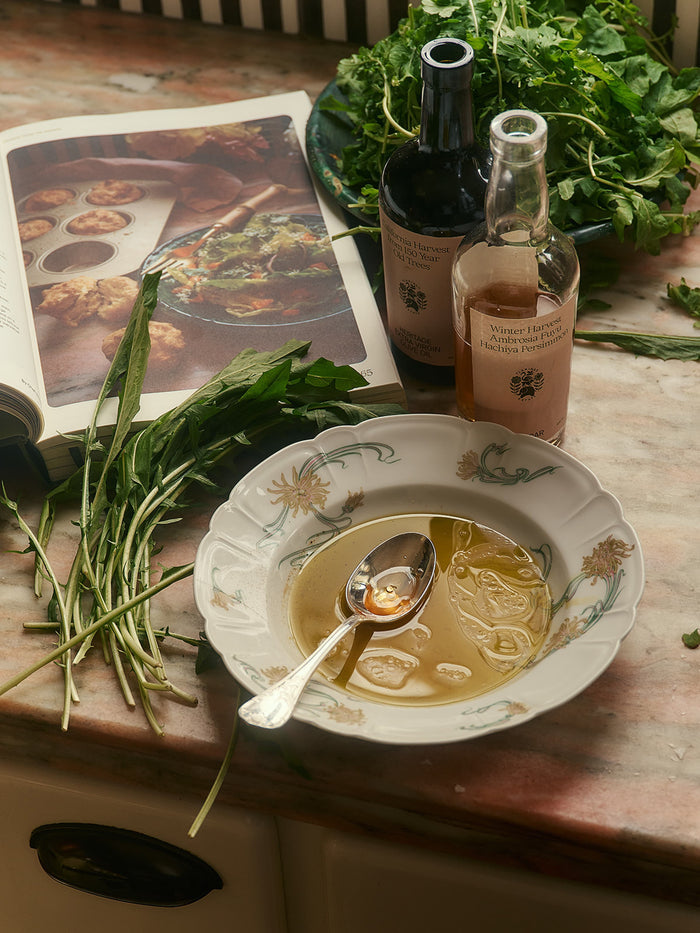 A decorative bowl with a spoon rests on a countertop, holding olive oil.