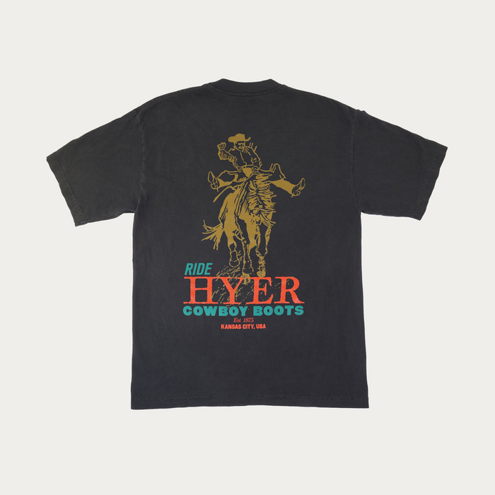 A faded black short-sleeve t-shirt shown from the back, featuring a large graphic print of a cowboy riding a bucking bronco. Below the graphic, the text reads 'RIDE HYER COWBOY BOOTS' in teal and orange-red lettering, with 'Est 1975' and 'KANSAS CITY, USA' printed underneath.
