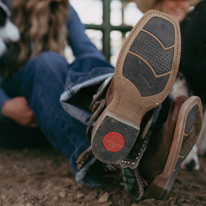 Close-up of brown rubber sole cowboy boots with a red heel cap logo on a blurred background