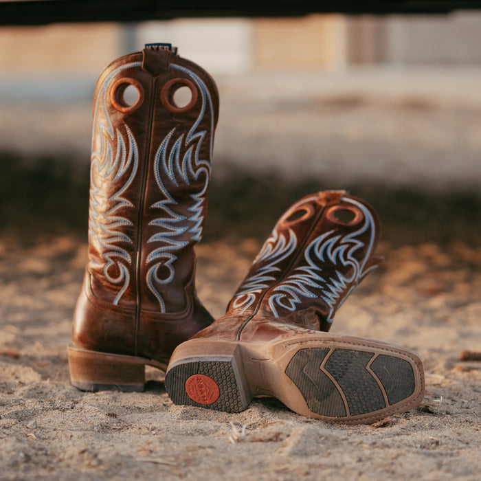 Pair of brown cowboy boots with white embroidery on a dirt ground.