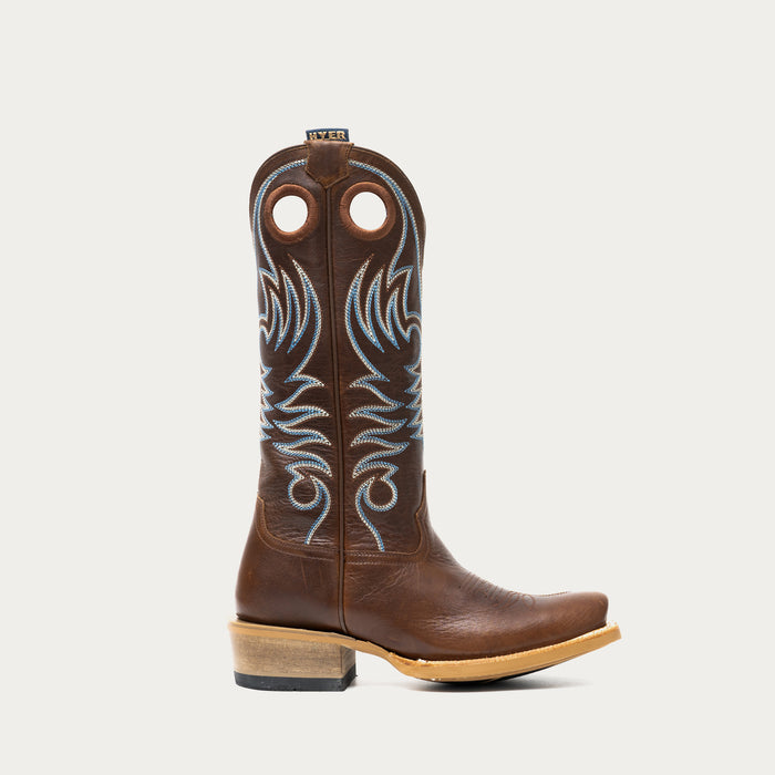 Brown cowboy boot with white and blue embroidery on a light gray background