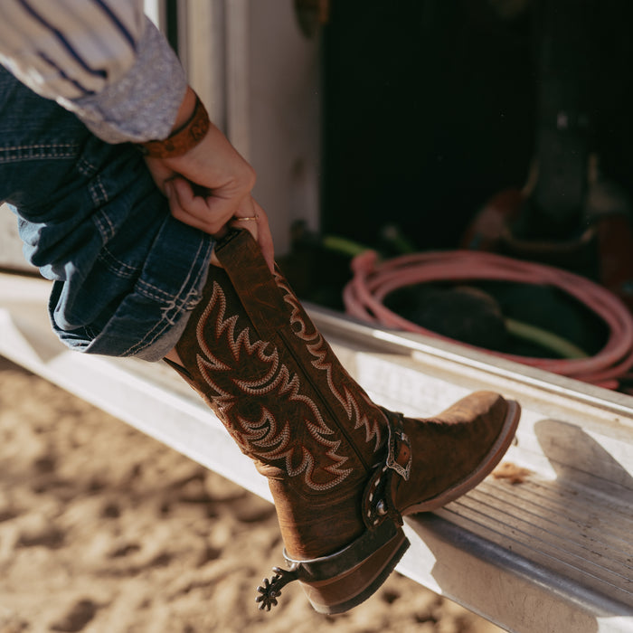 Person with foot up on ledge showing brown cowboy boot with intricate stitching and spur
